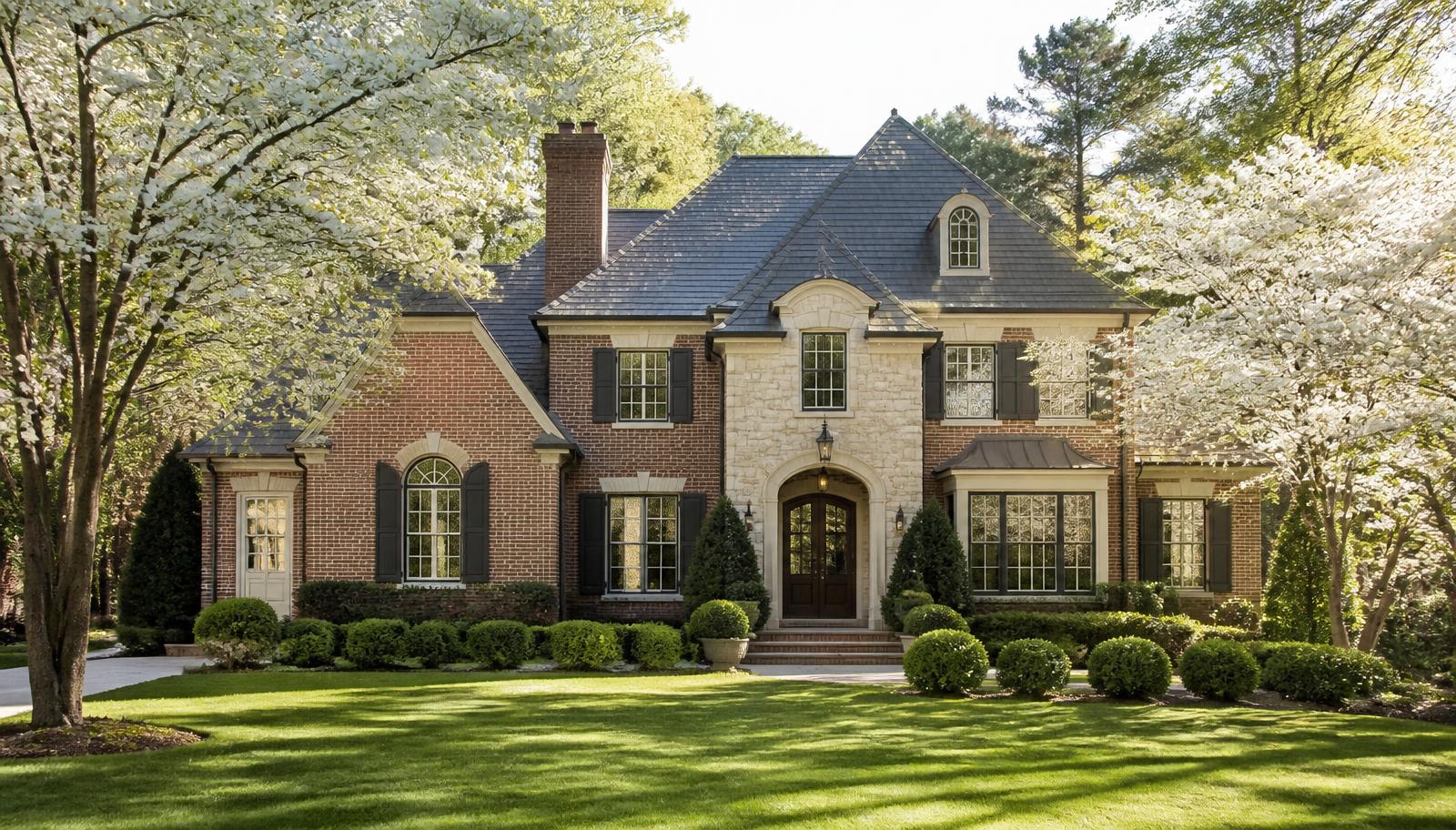 Brick and stone estate home with dogwoods in bloom on a leafy Atlanta street